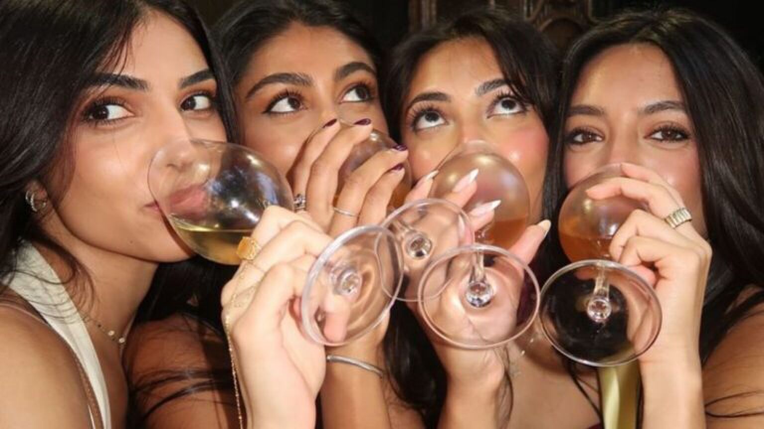 Vier vrouwen staan met wijnglazen in hun hand. Ze nemen een slok.