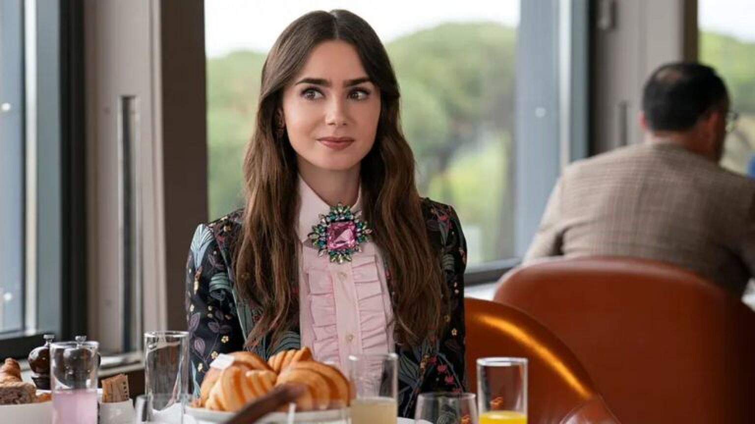 Emily uit Emily in Paris zit aan tafel.