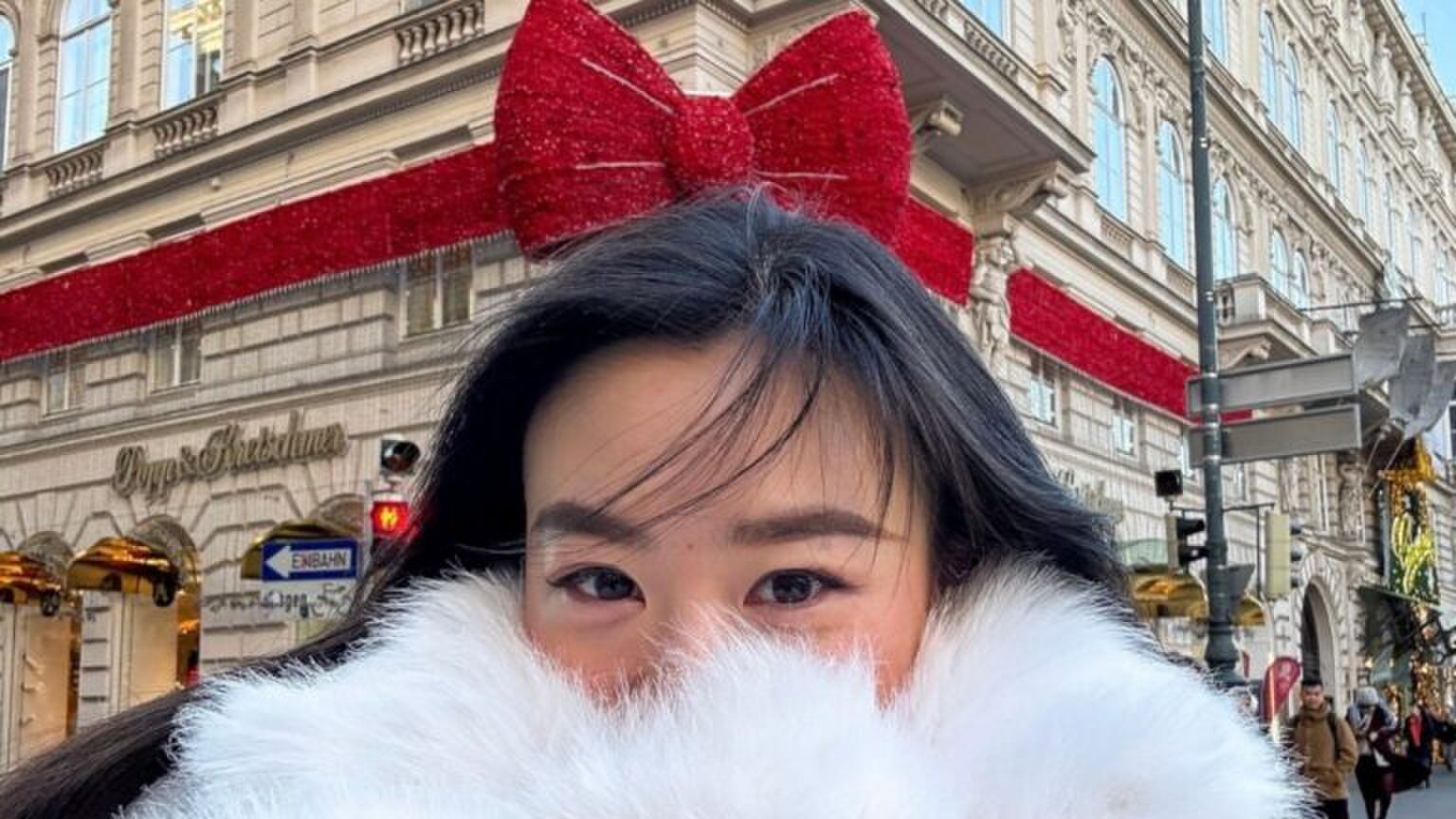 Een meisje staat voor een winkel waardoor het lijkt alsof ze een grote strik op haar hoofd heeft.