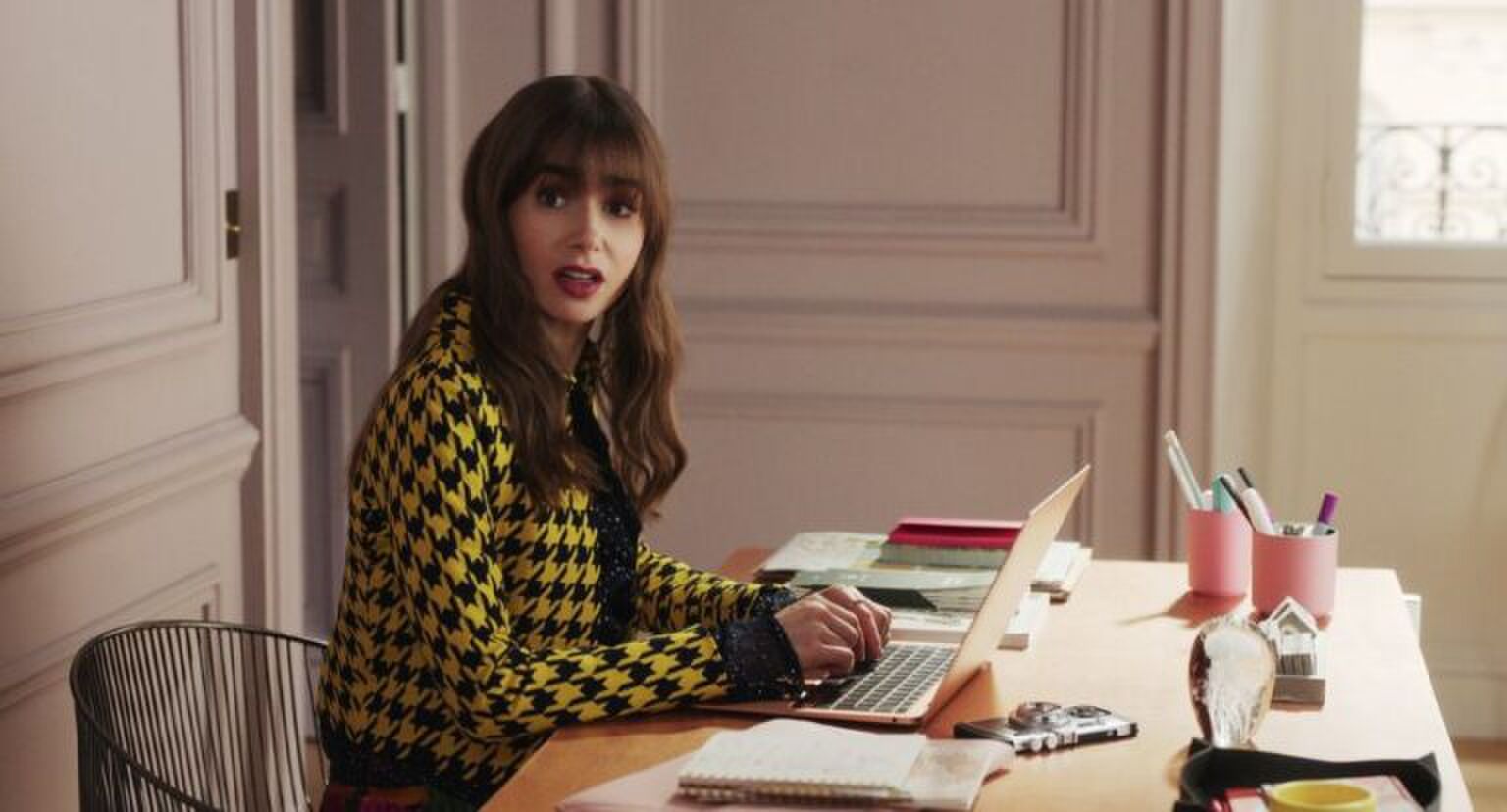 Sc&egrave;ne uit Emily in Paris waar Emily achter haar bureau zit.