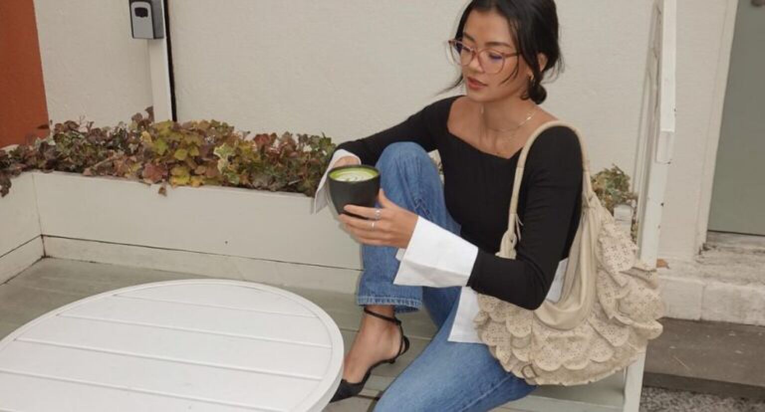 Een vrouw die op een bankje matcha zit te drinken.