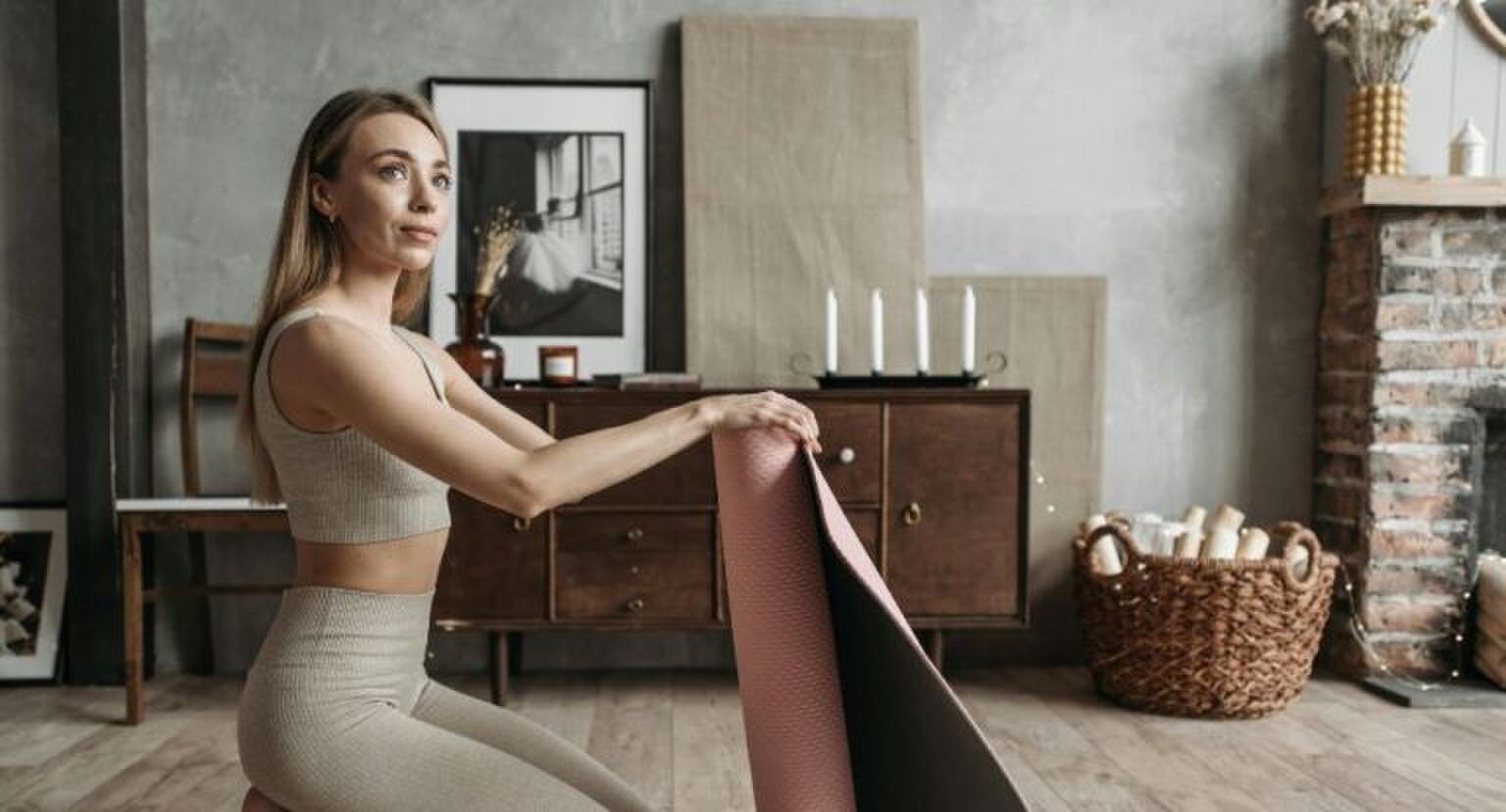 Een jonge vrouw zit in haar kamer met een yogamat.