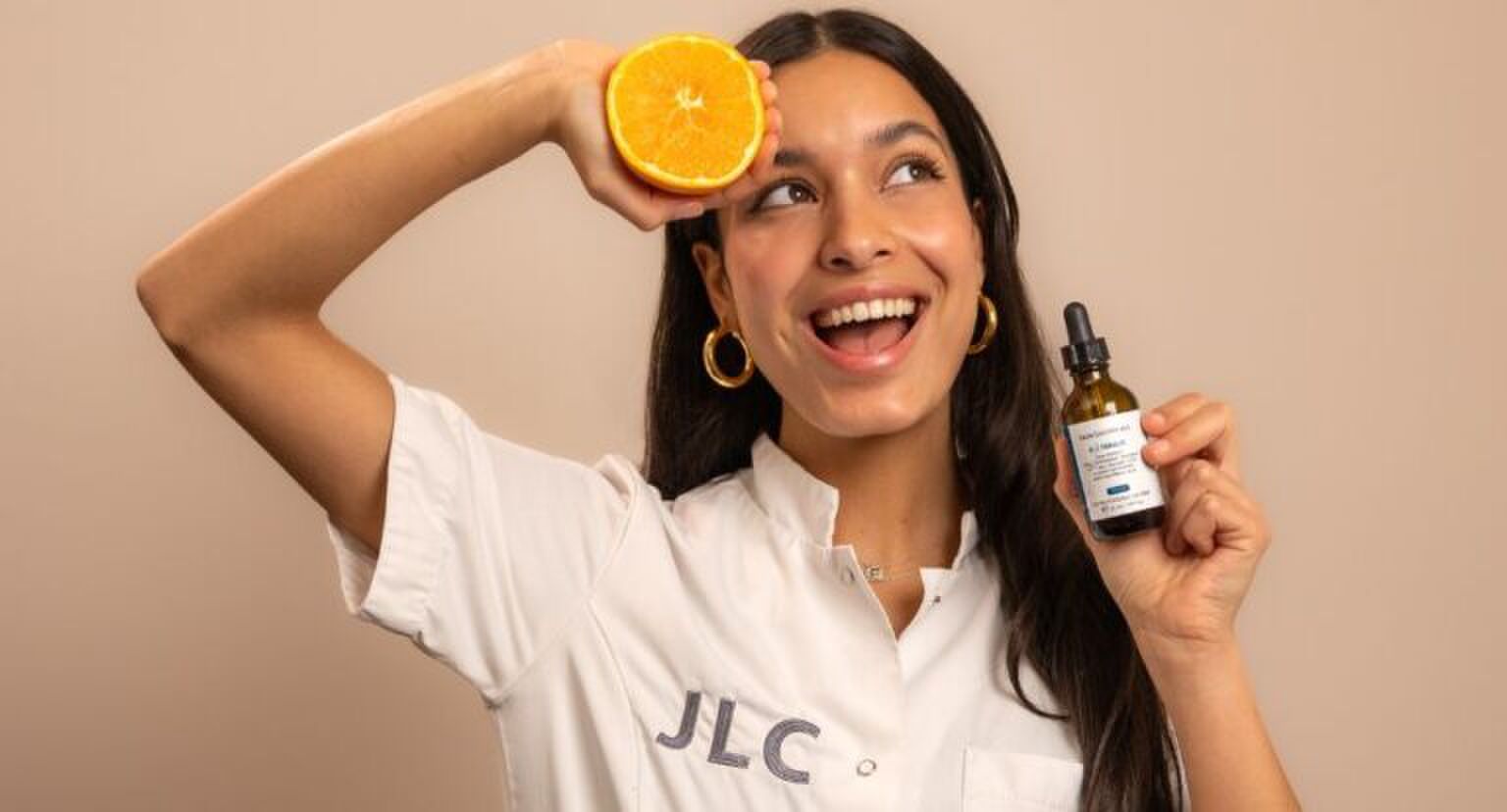 Jonge vrouw met een sinaasappel en een Vitamine C serum in haar handen.