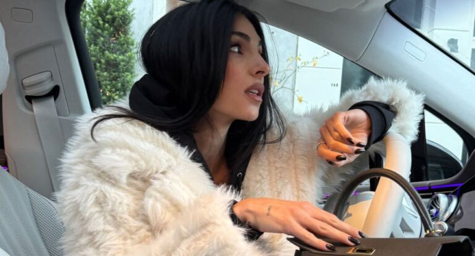 Anna Nooshin die in een auto zit, wegkijkt en naar haar tas reikt.