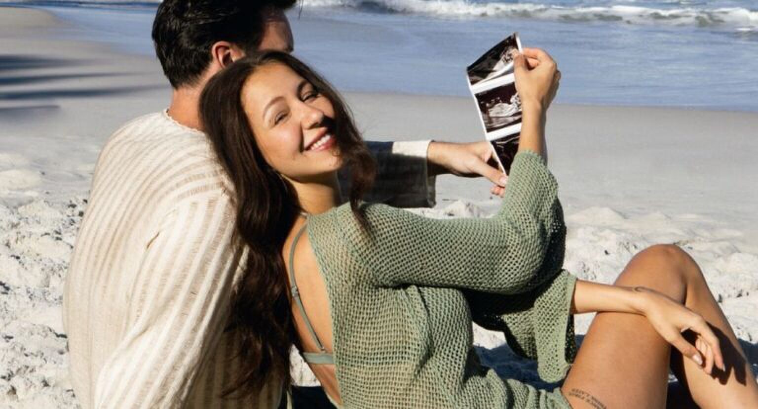 Sophie Milzink en haar vriend Brian zitten samen op het strand met een babyecho in de hand.