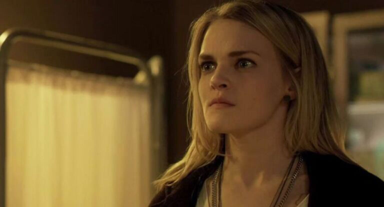 Een blonde vrouw kijkt met een serieuze blik langs de camera.