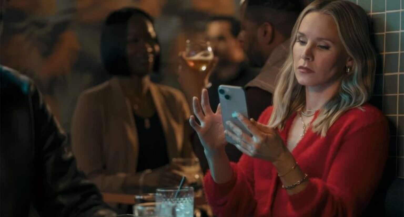 Kristen Bell kijkt vermoeid naar haar telefoon.