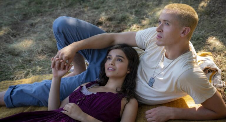 Meisje en jongen liggen hand in hand op de grond in een bos.