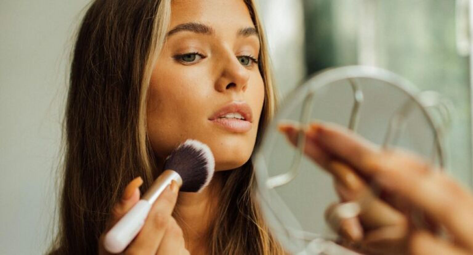 Een vrouw die haar make-up aan het doen is terwijl ze in een spiegel kijkt.