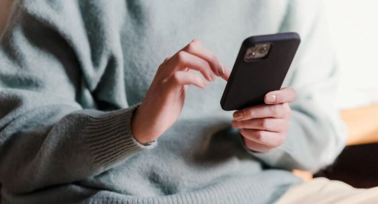 Een vrouw in een groene trui die op haar telefoon aan het scrollen is.