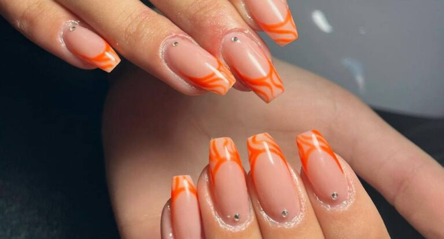 Twee handen met oranje nailart op de nagels.