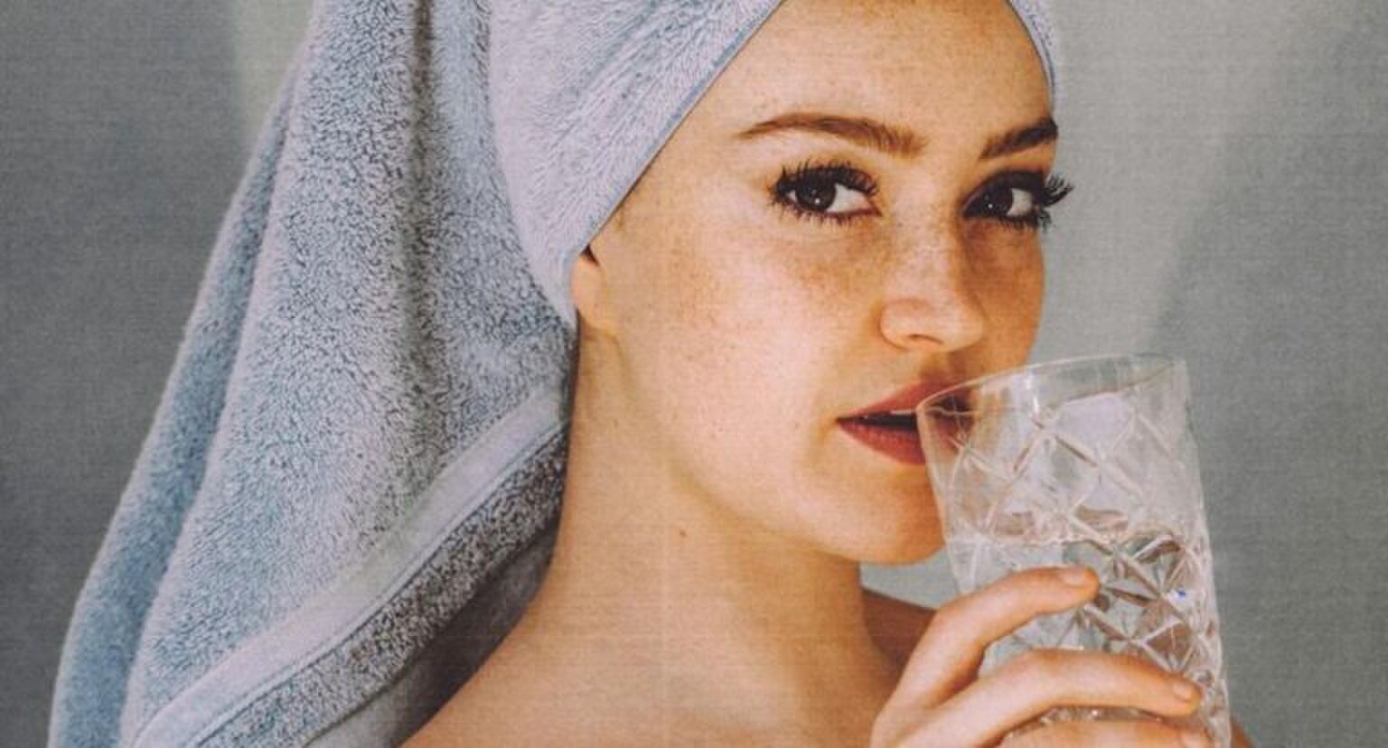 Een vrouw die water drinkt, met een handdoek op haar hoofd.