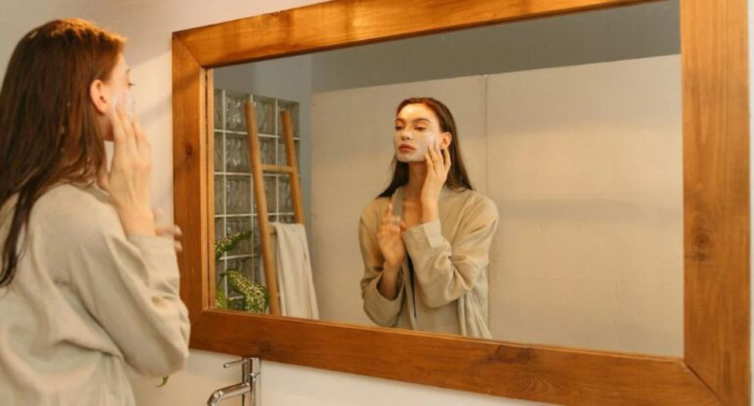 Een vrouw die in een spiegel kijkt terwijl ze een masker aanbrengt op haar gezicht.