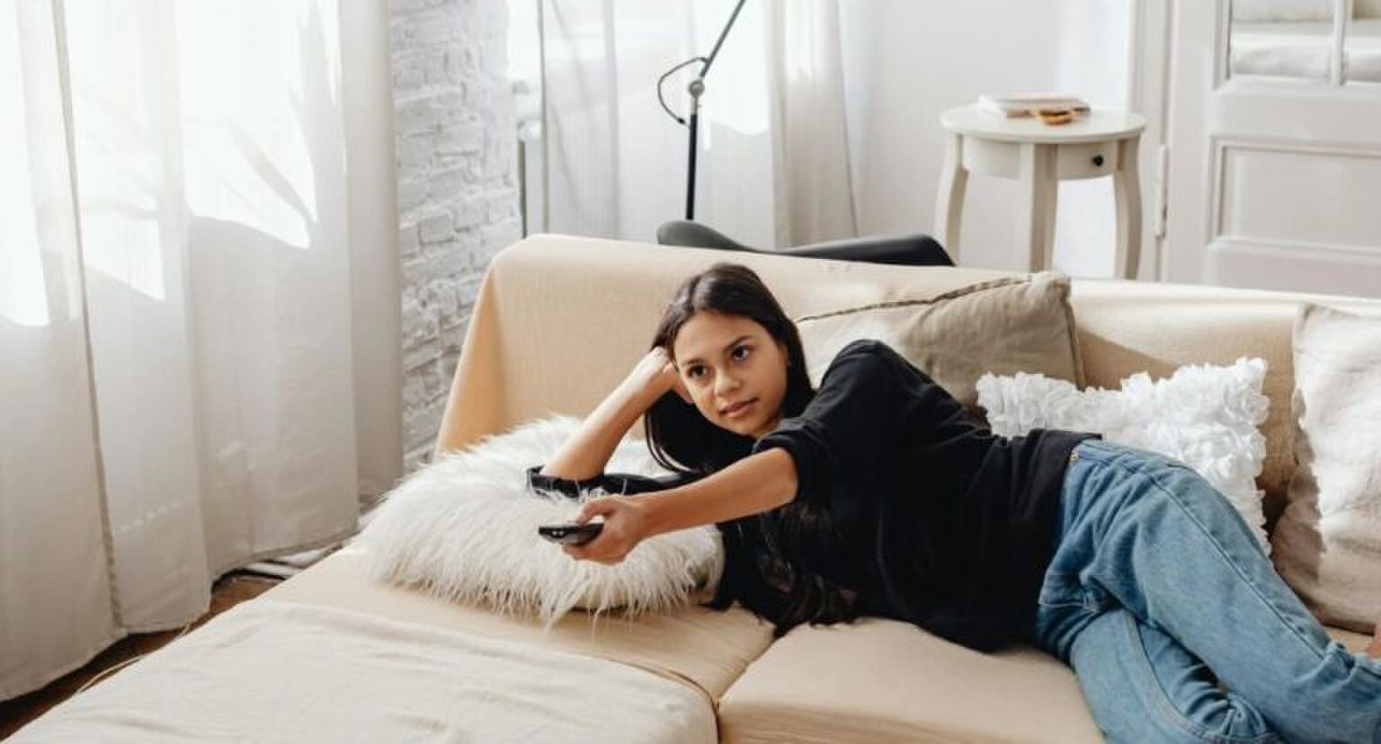Een meisje die op de bank ligt terwijl ze tv kijkt.