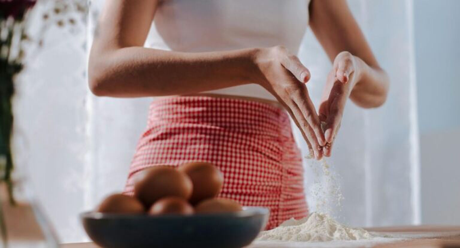 Een vrouw die aan het bakken is en bloem over het aanrecht strooit.