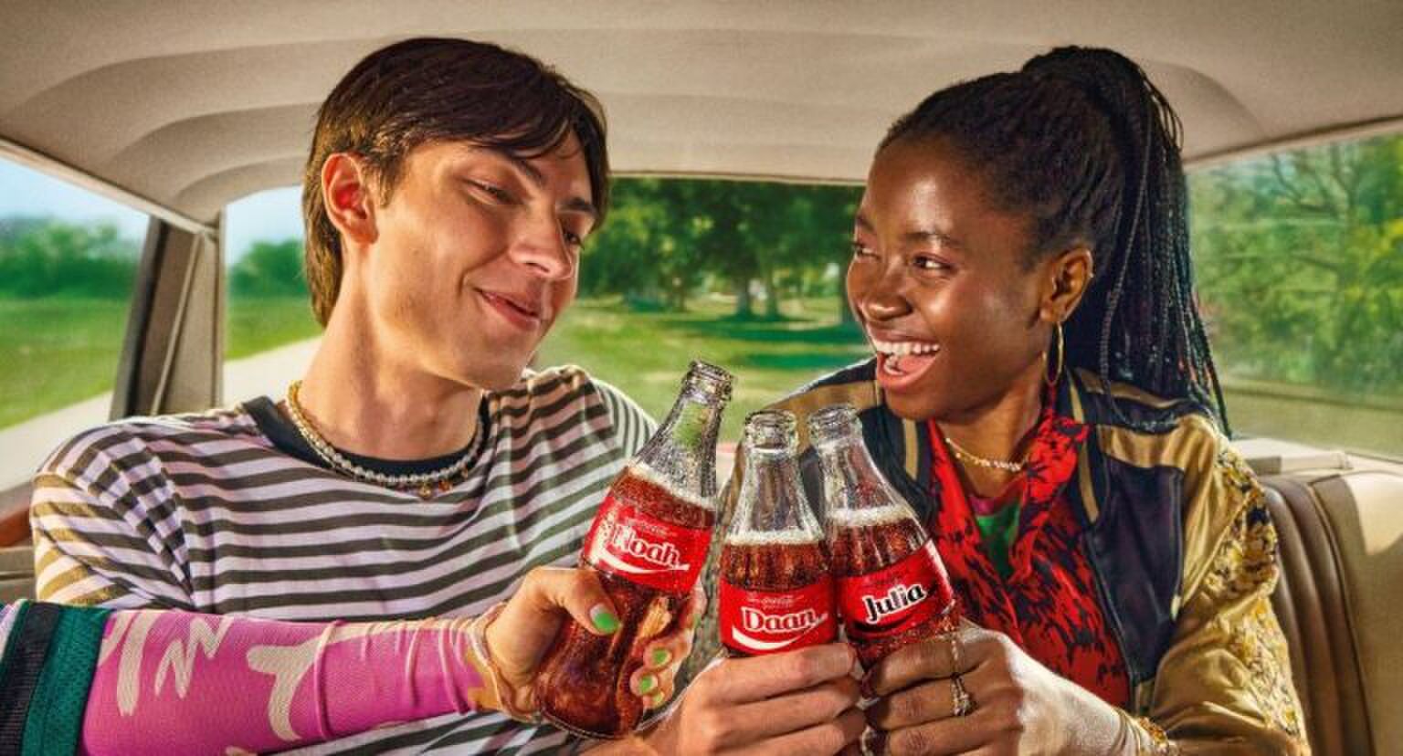 Een vrouw en een man die hun Coca-Cola flesje proosten.