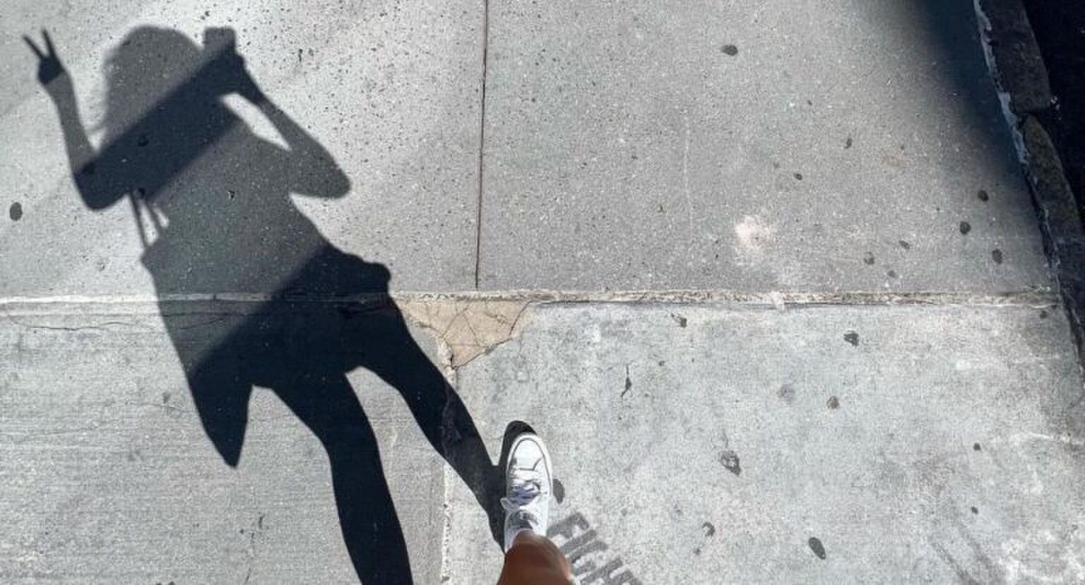 Ashley Alexander die aan het wandelen is en een selfie maakt van haar schaduw, terwijl ze een peace teken opsteekt.