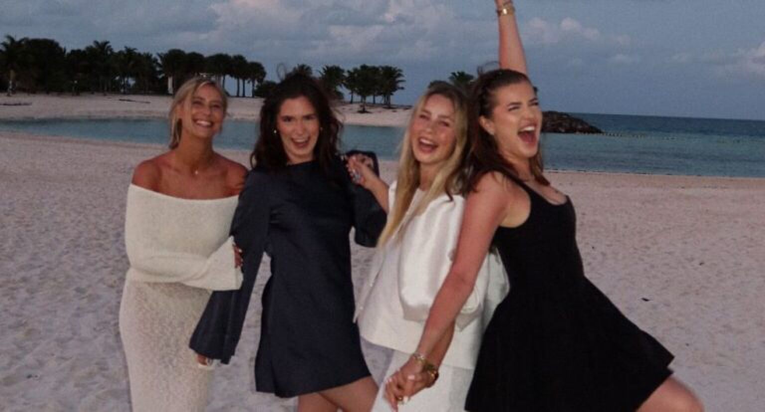 Vier meiden poseren lachend naast elkaar op het strand.