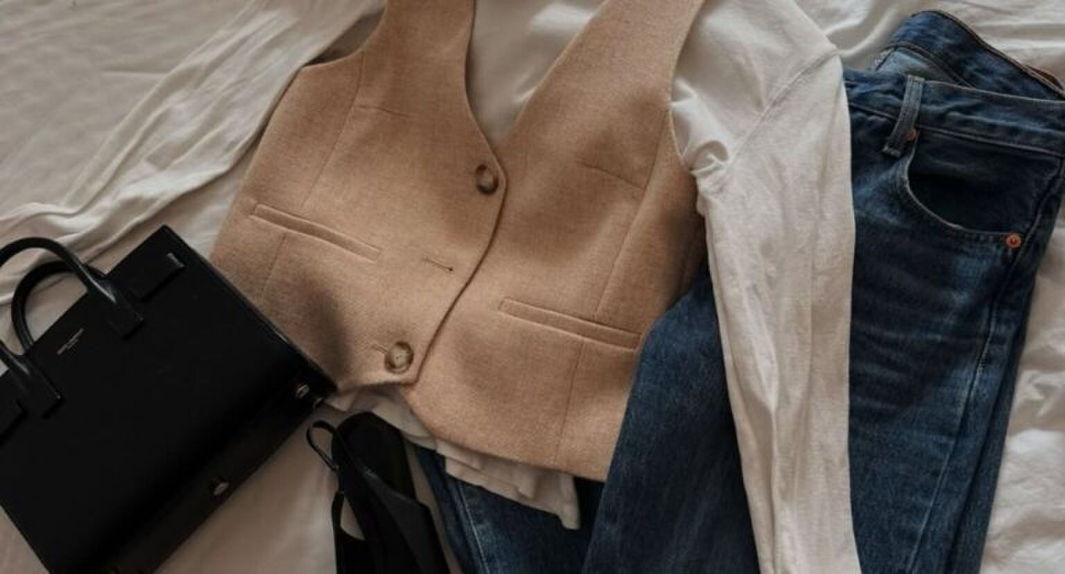 Kledingstukken en een tasje op een bed.