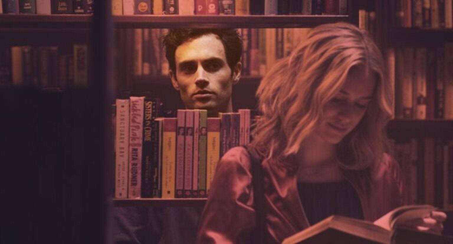 Man die door een boekenkast stiekem naar een vrouw kijkt.