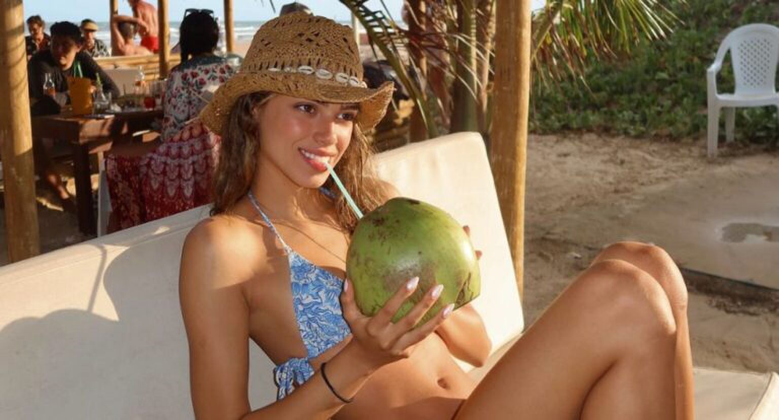 Een vrouw die op een strandbedje uit een kokosnoot drinkt.