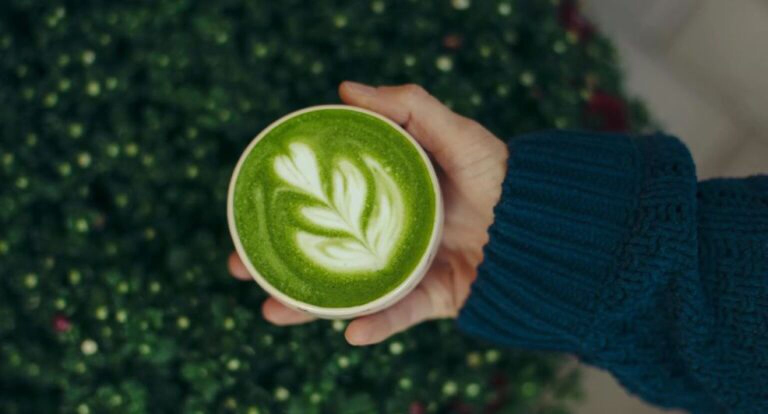 Een hand houdt een kopje matchakoffie vast.