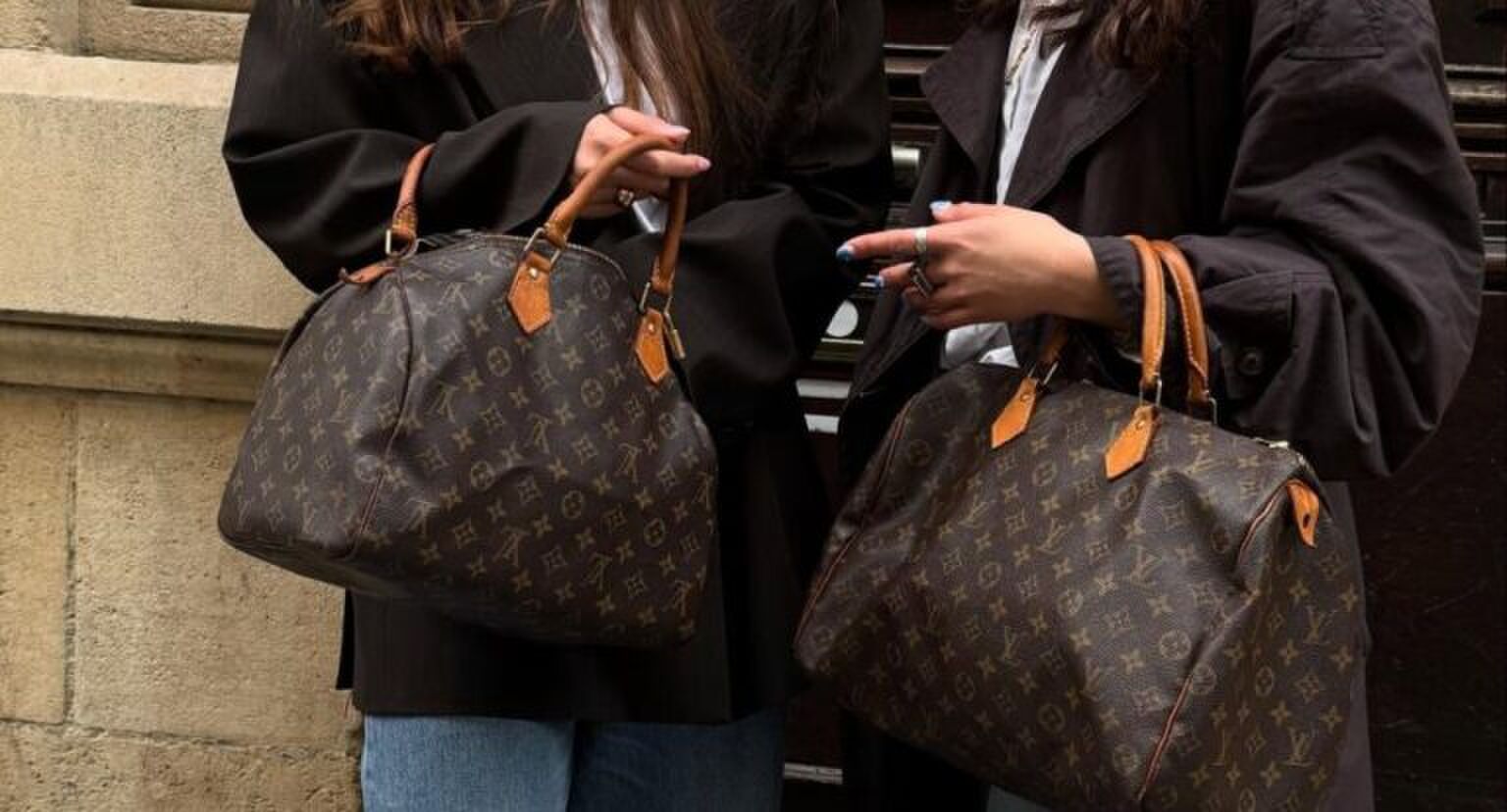 2 meiden die naast elkaar staan met allebei een grote Louis Vuitton tas in hun handen.