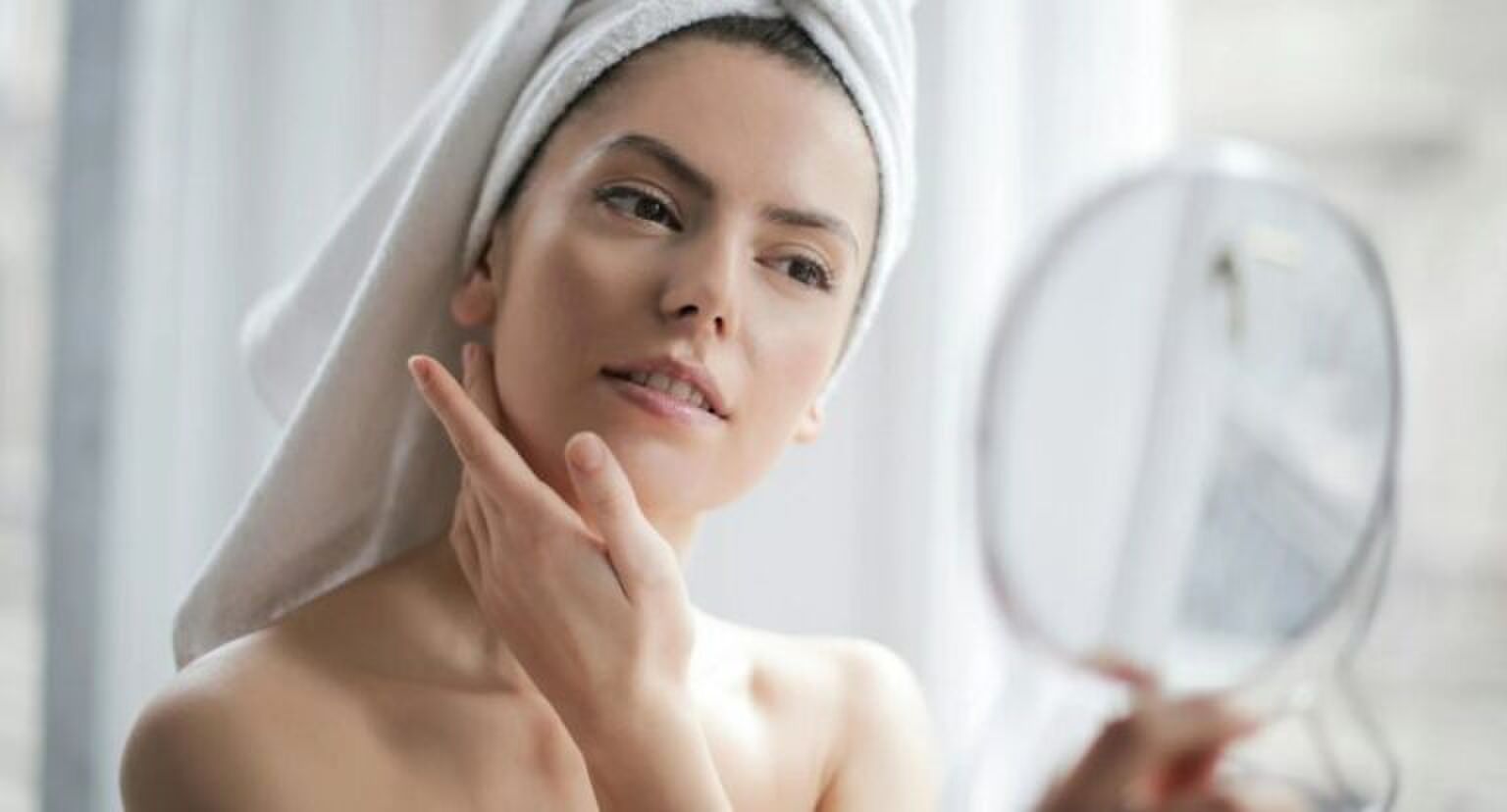 Vrouw bekijkt haar huid in een handspiegel.