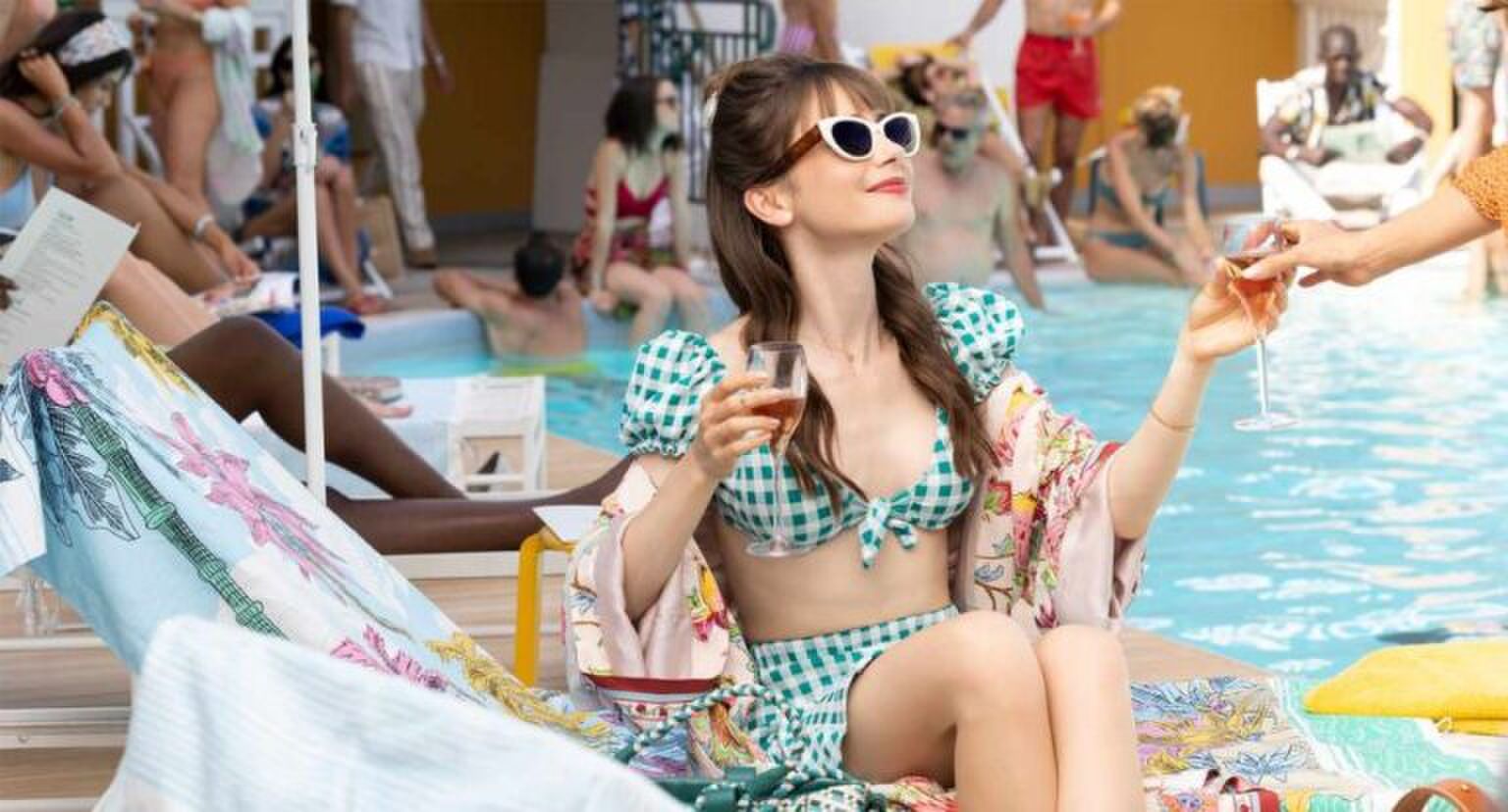 Sc&egrave;ne uit Emily in Paris waar Emily aan het zwembad ligt en een drankje aanneemt.