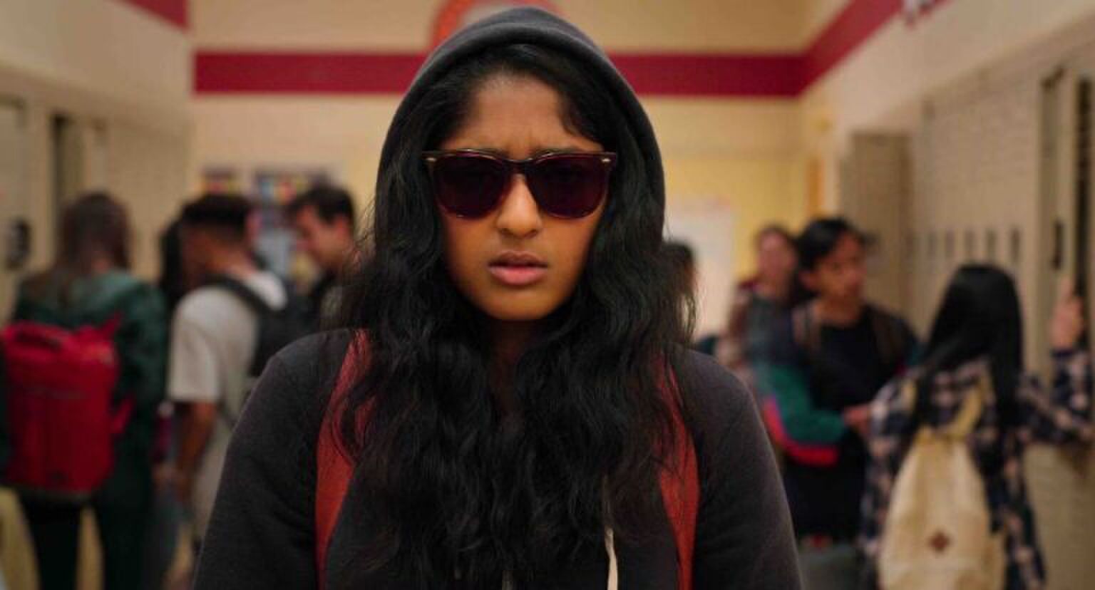 Sc&egrave;ne uit Never Have I Ever waar Devi met capuchon omhoog en zonnebril op door de schoolgangen loopt.