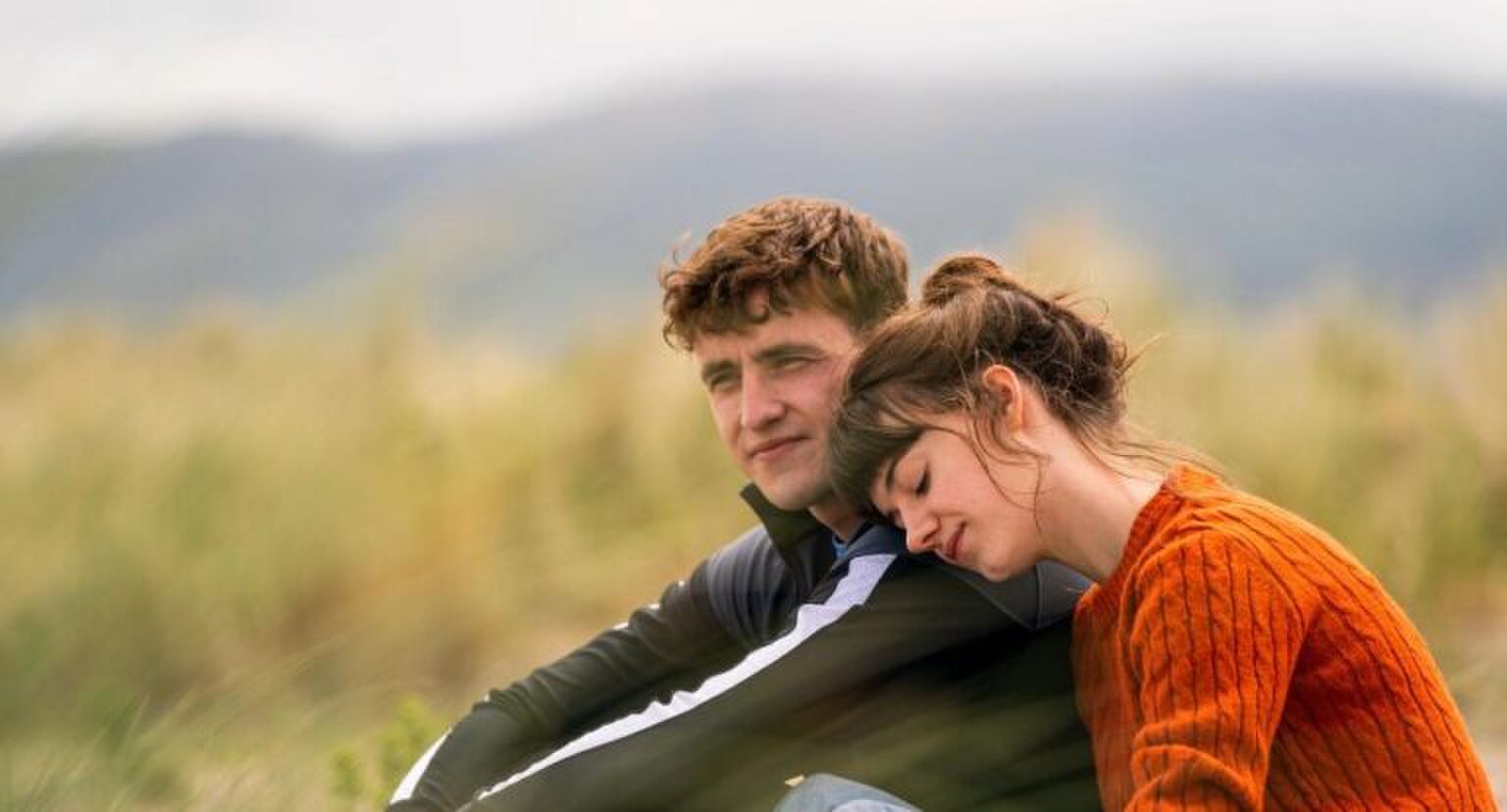 Een vrouw ligt met haar hoofd op de schouder van een man terwijl ze buiten zitten.