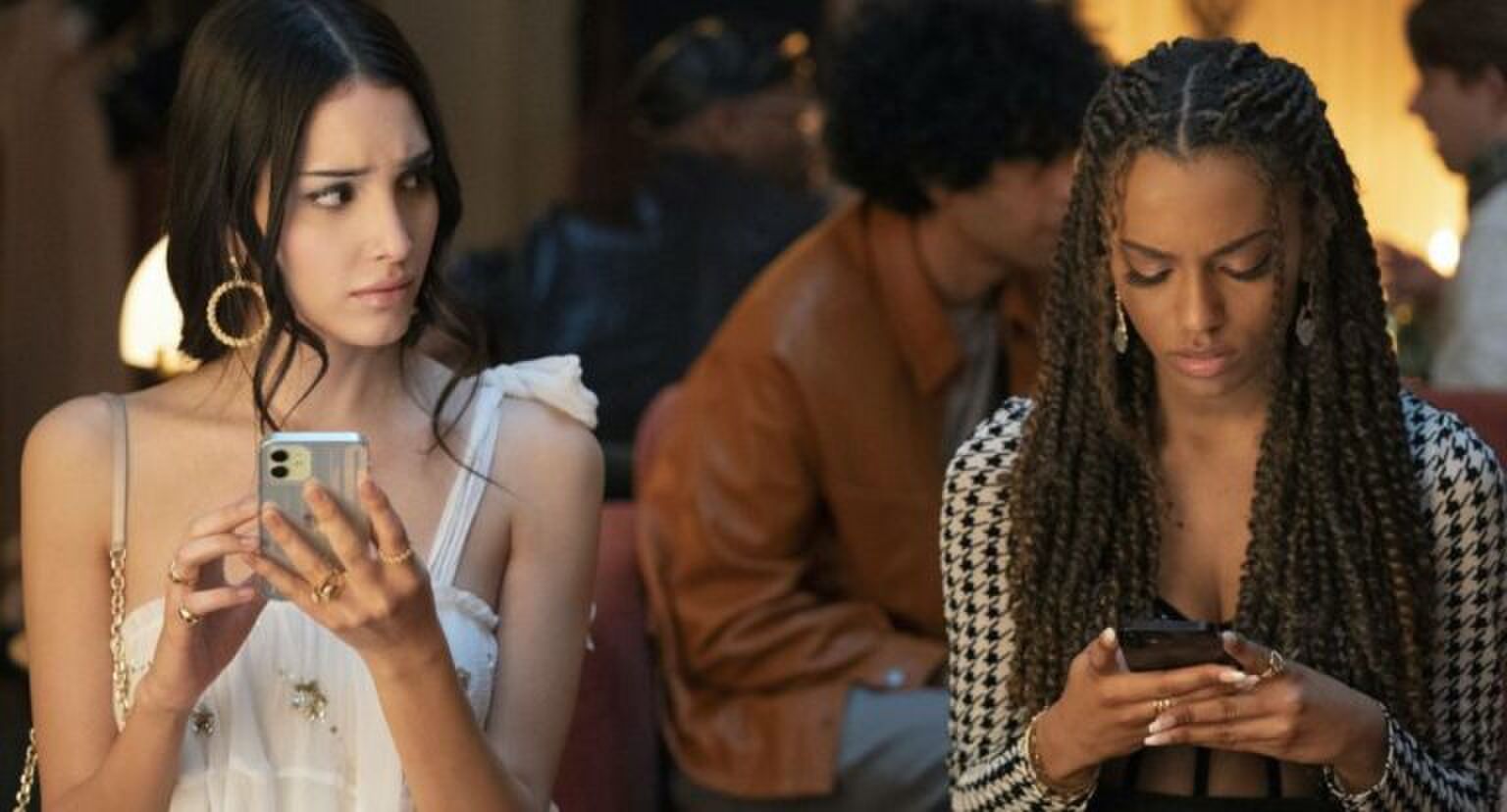 Twee meisjes zitten op hun telefoon, de een kijkt de ander geschrokken aan.