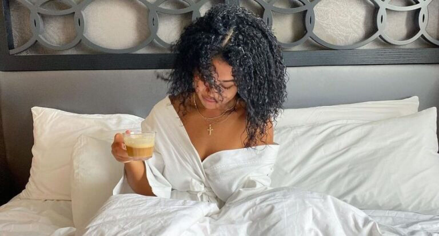 Een vrouw die in bed zit met een koffie in haar hand.