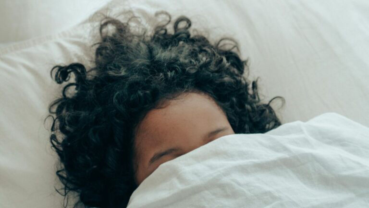 Een kind ligt onder de dekens in bed.