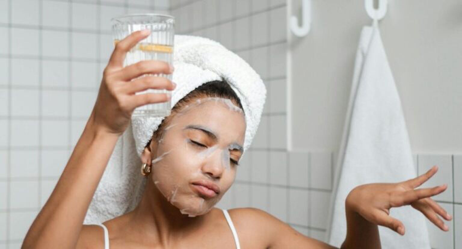 Jonge vrouw staat met een glas water in de badkamer.