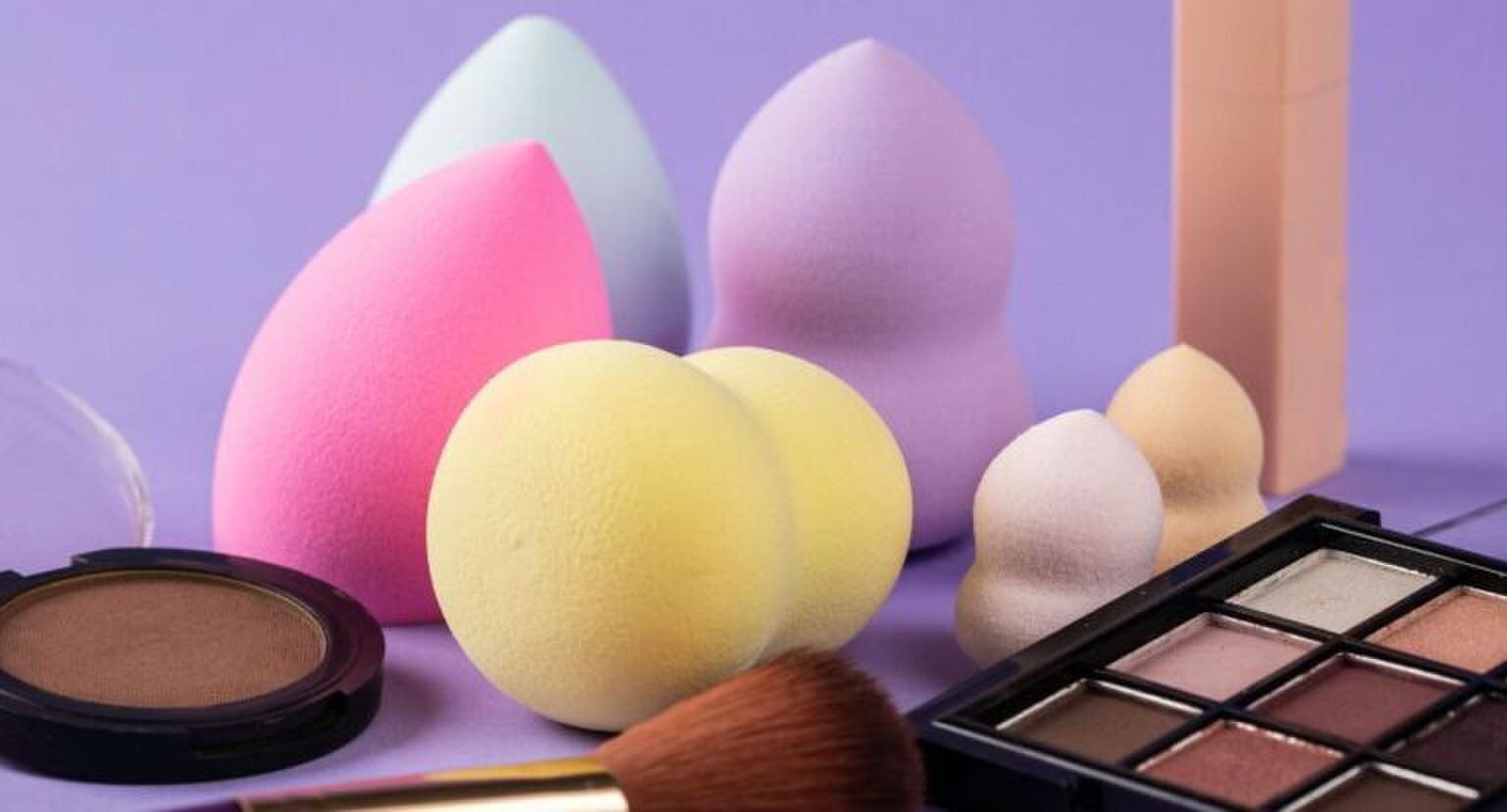 Beautyblenders en andere make-up producten op een paarse achtergrond.