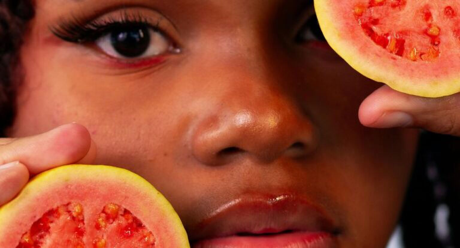 Meisje die guave's voor haar gezicht houdt.