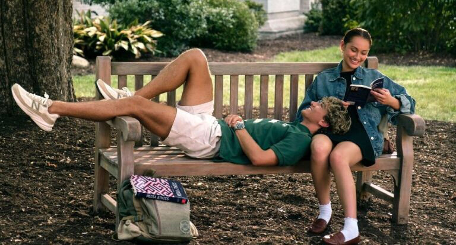 Meisje leest een boek op een bankje en een jongen ligt op haar schoot.