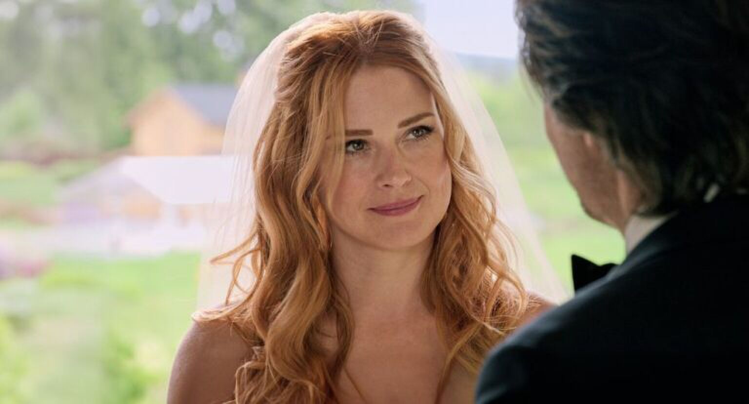 Vrouw in bruidsjurk kijkt verliefd naar man buiten beeld.