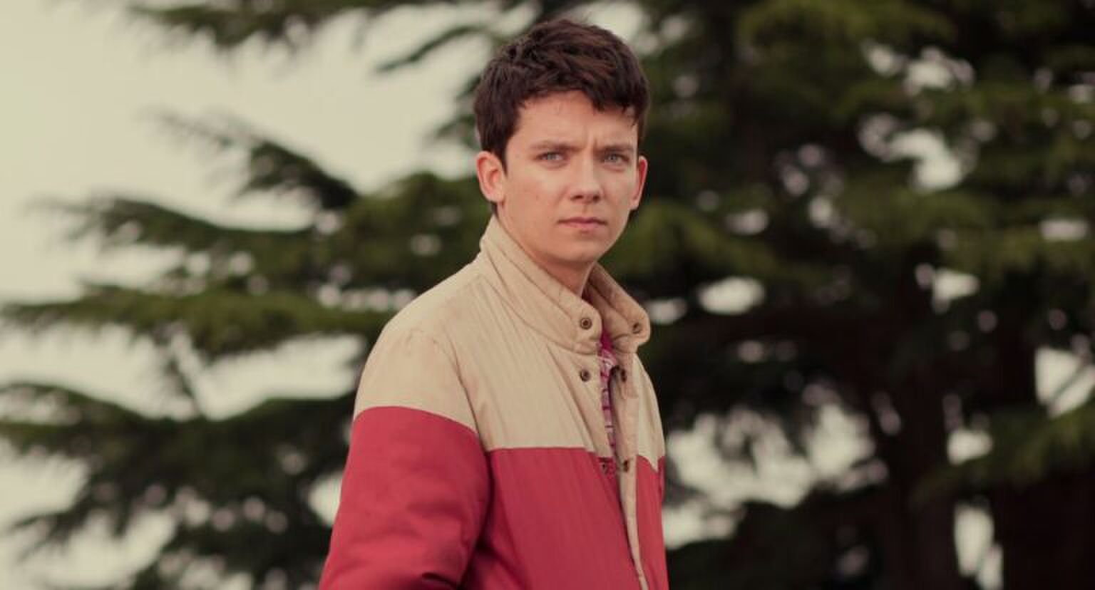 Jongen staat alleen voor bosjes en staart achter de camera.