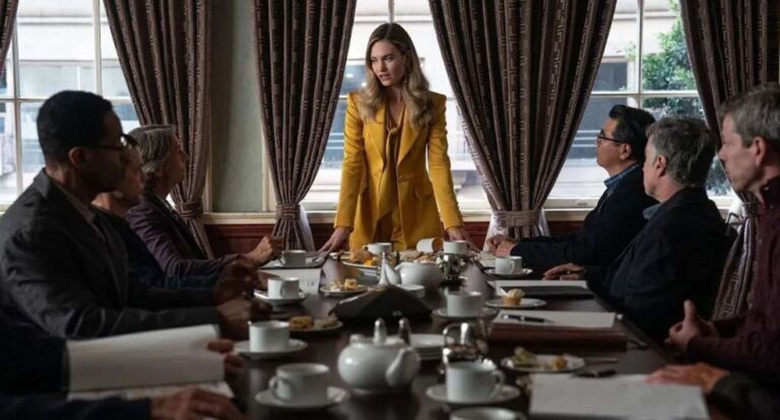 Vrouw staat aan het hoofd van een vergadertafel met mannen om haar heen.