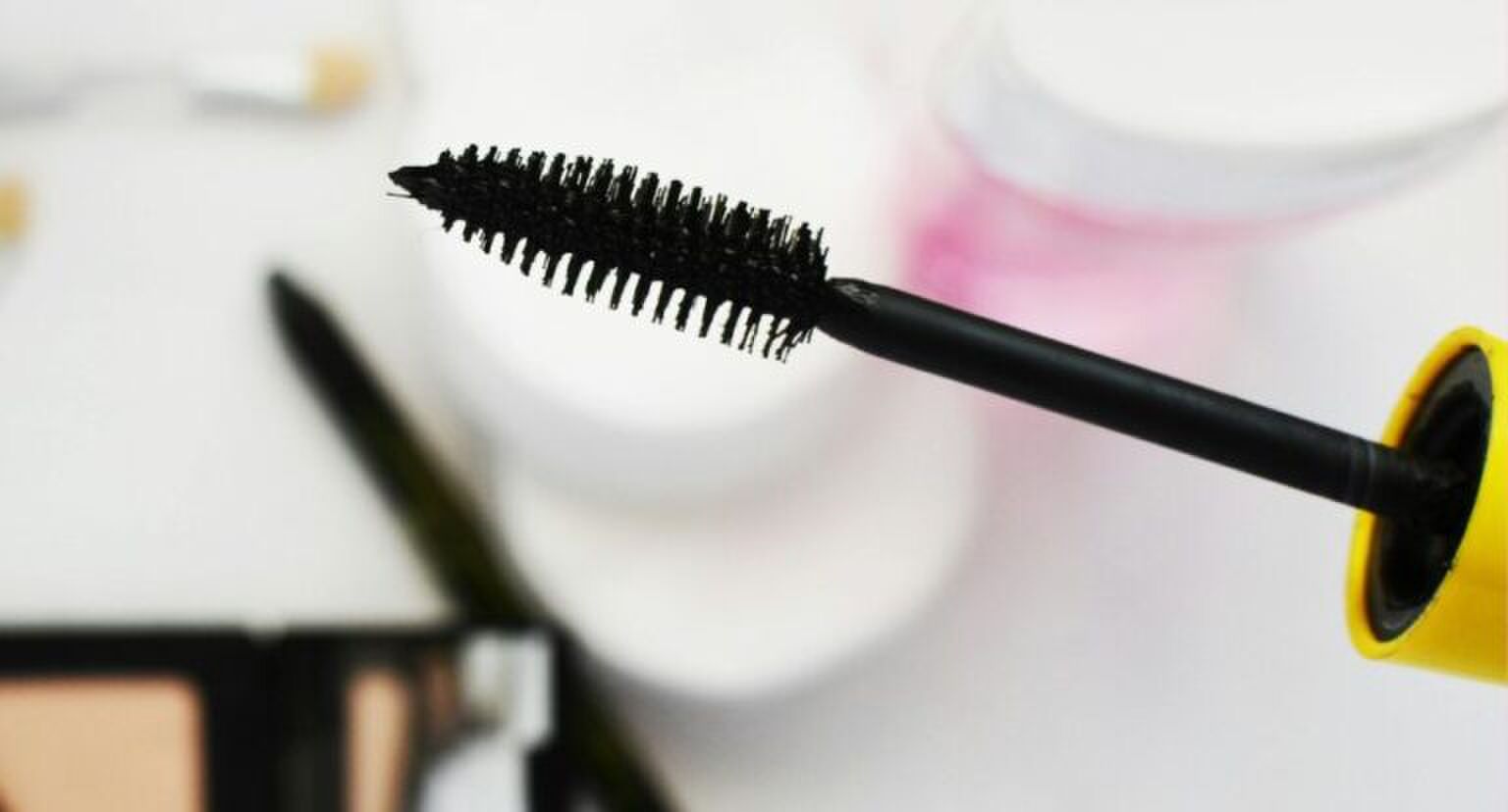 Mascaraborsteltje boven een witte tafel met andere beautyproducten.