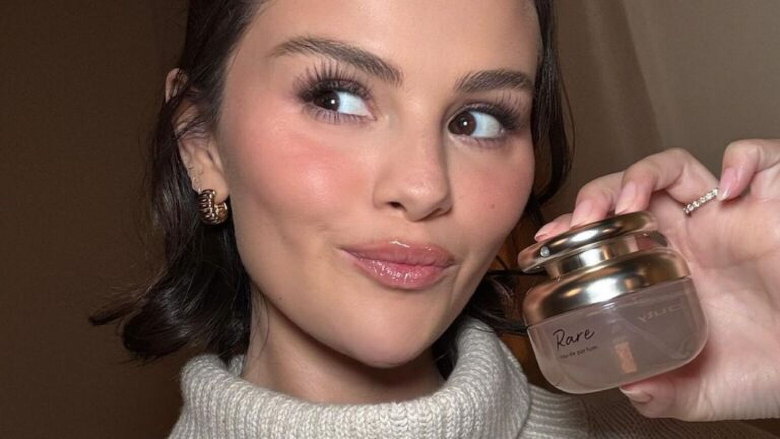 Een selfie van Selena Gomez die Rare Beauty's eerste parfum, Rare Eau de Parfum, vasthoudt.