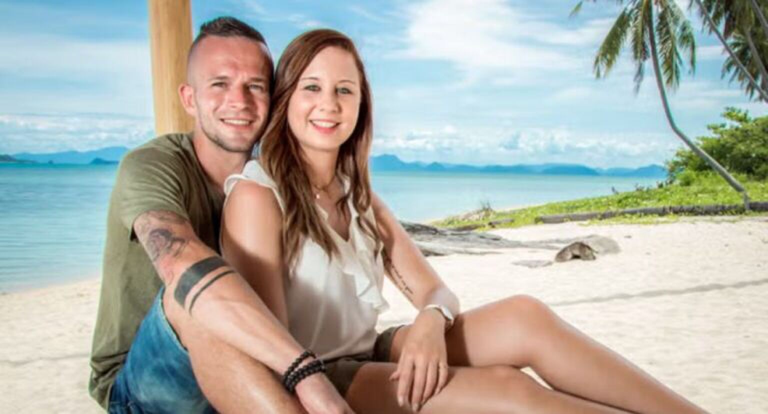 Jongen en meisje zitten tegen elkaar aan op een strand.