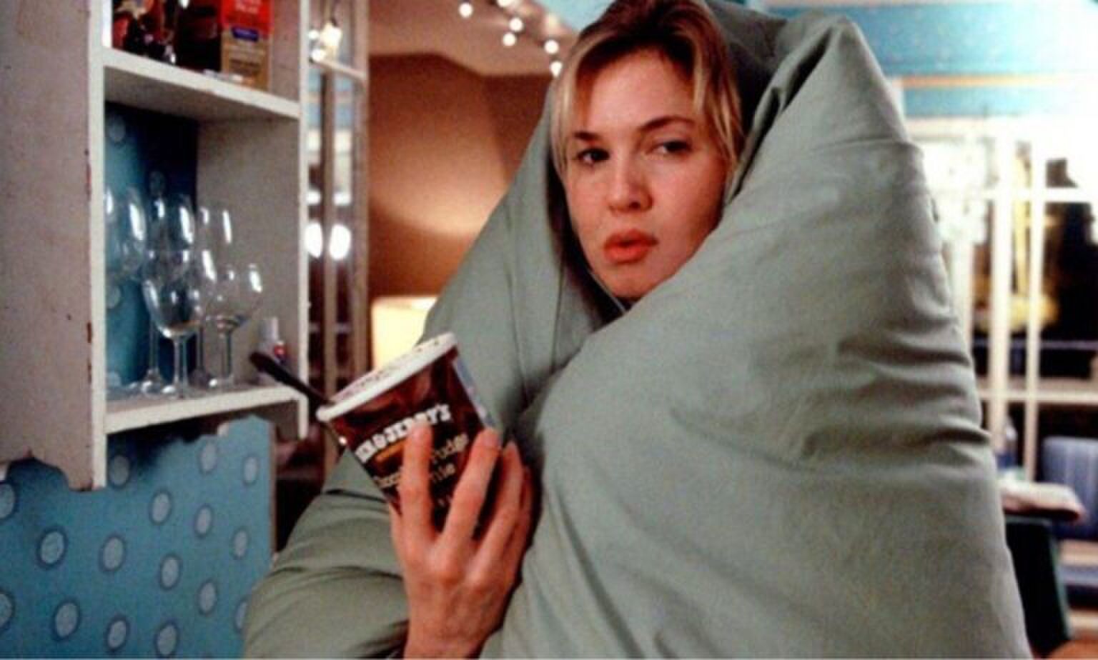 Luie vrouw, zit verwikkeld in een deken met een bak ijs in haar hand. Ze kijkt verveeld. Bridget Jones