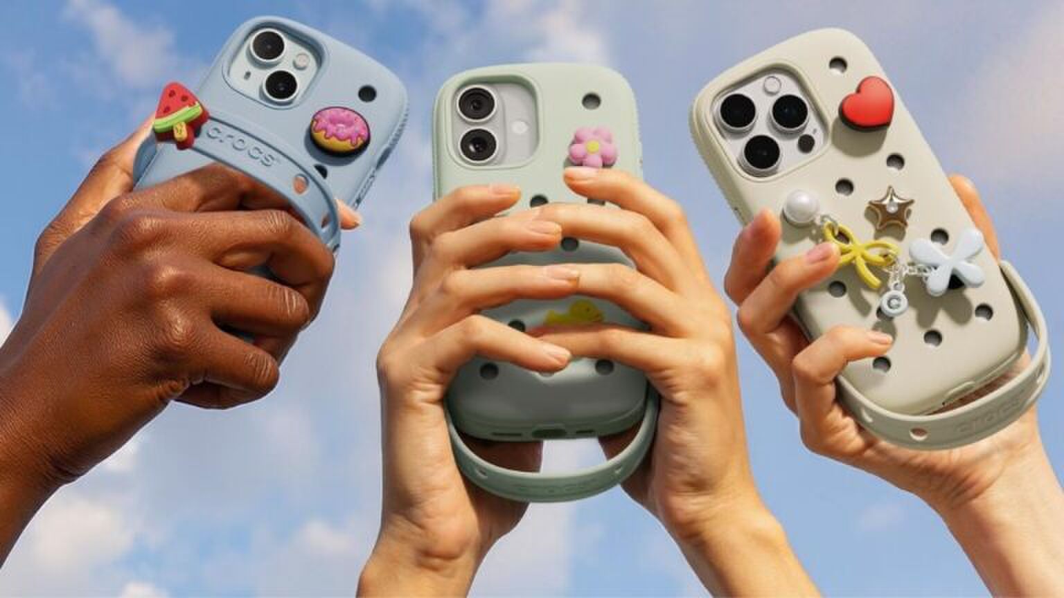 Drie verschillende telefoonhoesjes worden vastgehouden door drie verschillende armen. De telefoonhoesjes zijn van het merk: Crocs in samenwerking met SLBS.