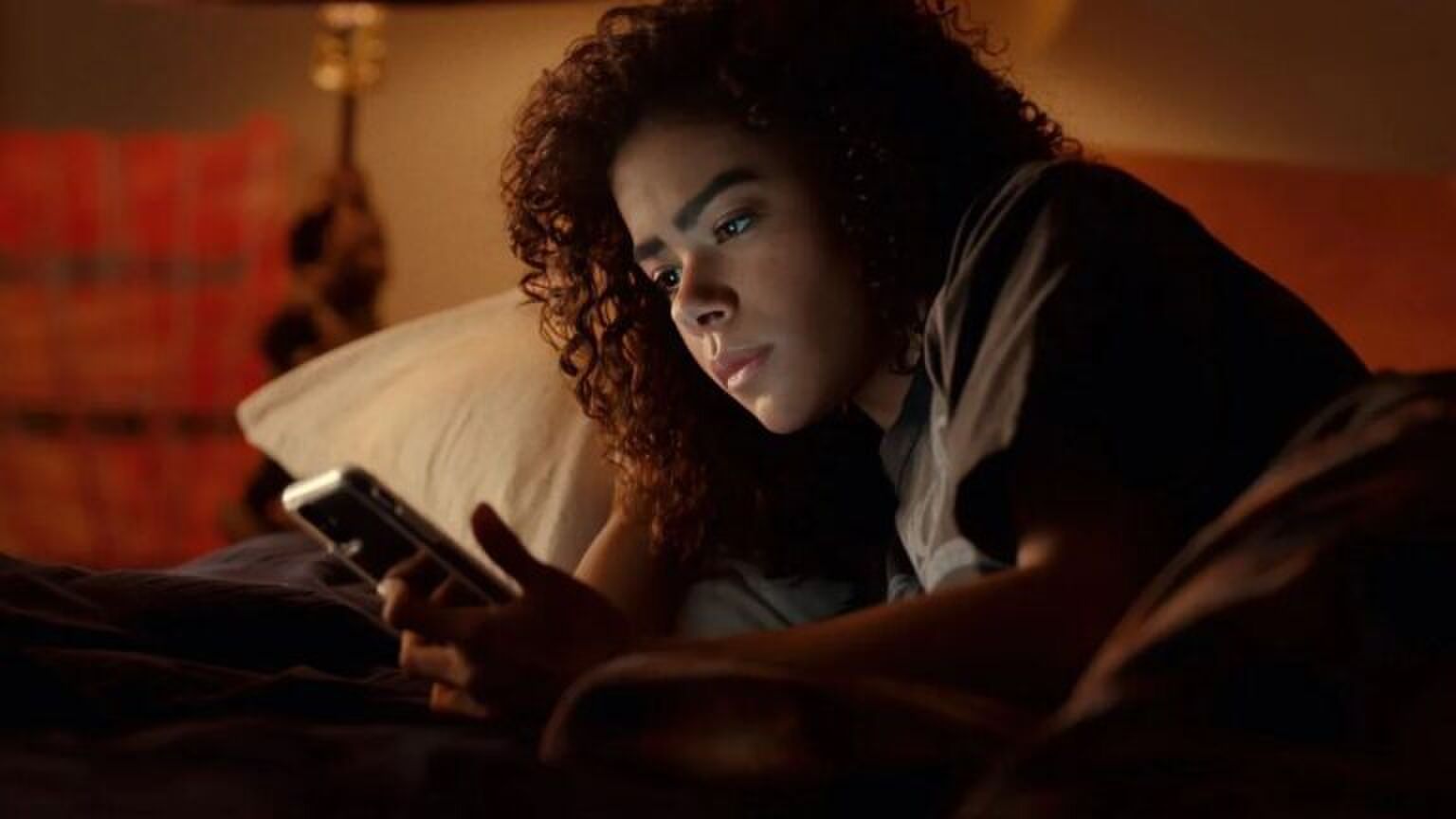 Vrouw kijkt op telefoon. Ze ligt in bed. Ze kijkt verbaasd. Afbeelding uit: Ginny and Georgia.