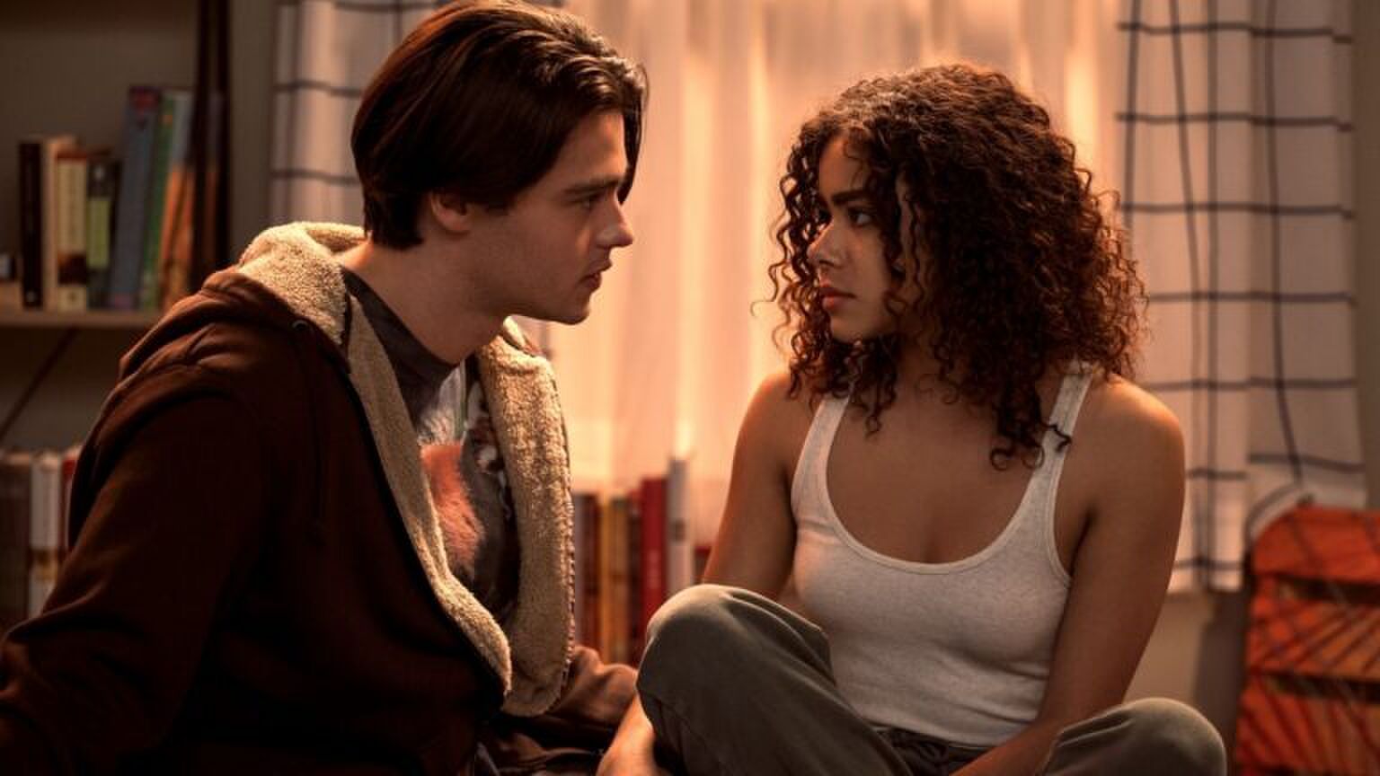 Een jongen en meisje zitten samen op bed en kijken elkaar aan.