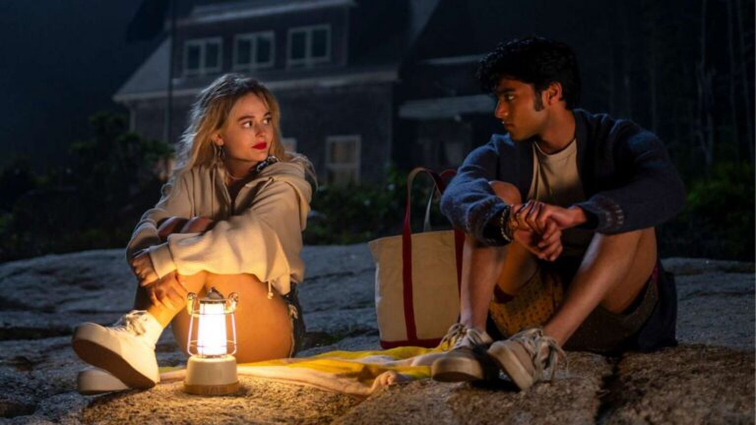 Een man en vrouw zitten op het strand in het donker. Er brandt een lantaarn. Afbeelding uit: We Were Liars.