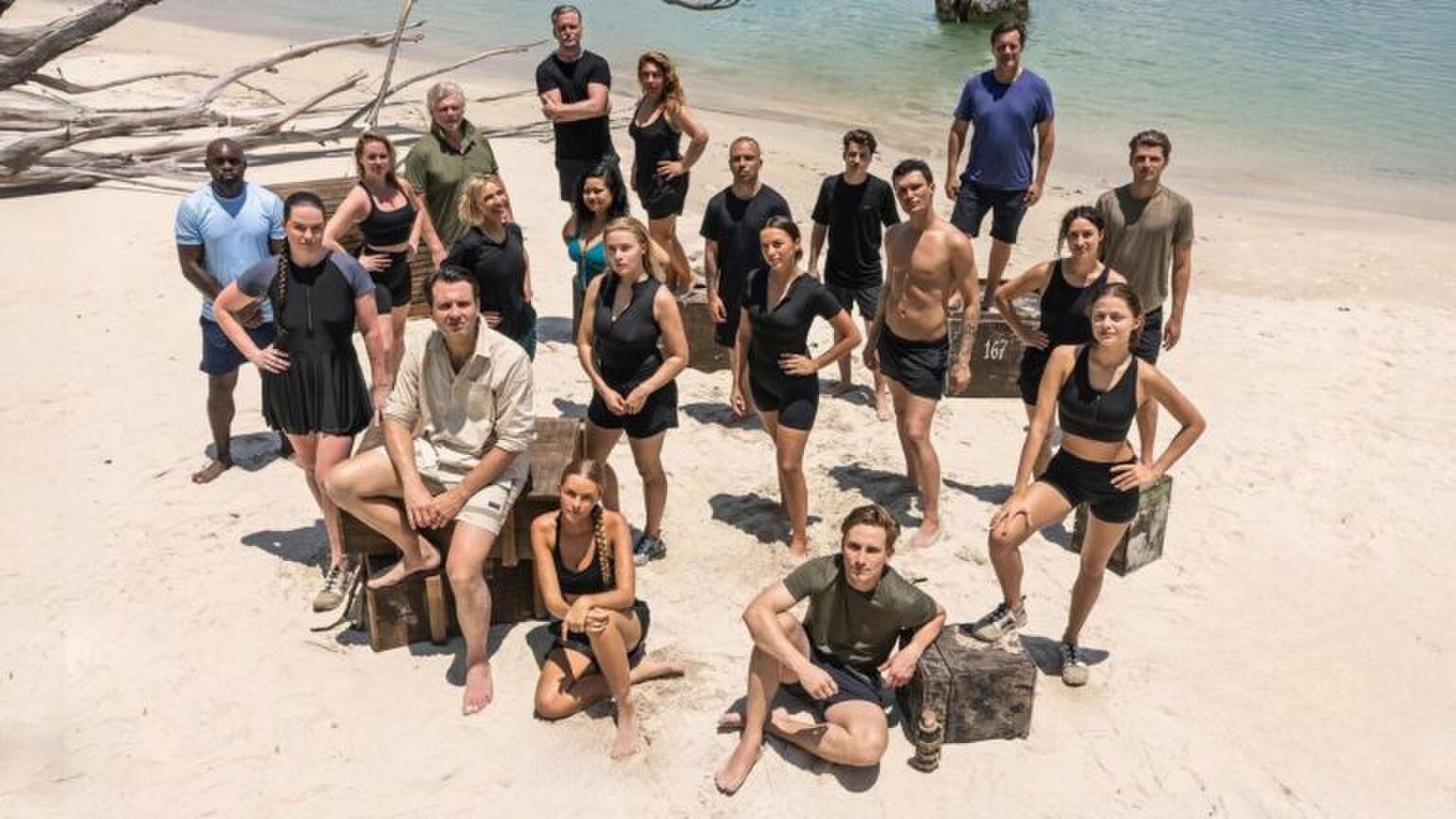 Expeditie Robinson deelnemers staan op een tropisch eiland. Ze kijken stoer omhoog.